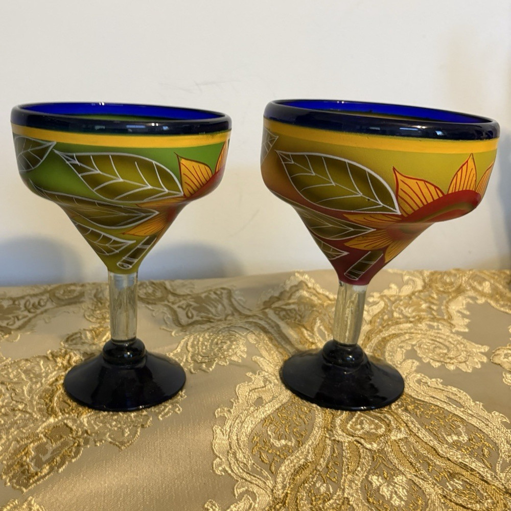 A pair of hand-painted glass margarita glasses with floral and leaf motifs.