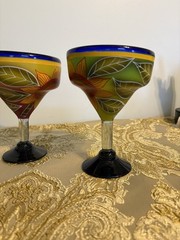 A pair of hand-painted glass margarita glasses with floral and leaf motifs.