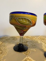 A pair of hand-painted glass margarita glasses with floral and leaf motifs.