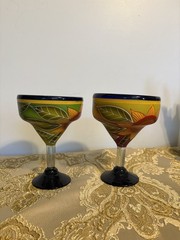 A pair of hand-painted glass margarita glasses with floral and leaf motifs.