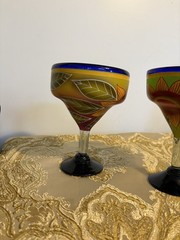 A pair of hand-painted glass margarita glasses with floral and leaf motifs.