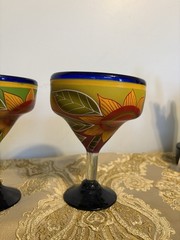 A pair of hand-painted glass margarita glasses with floral and leaf motifs.