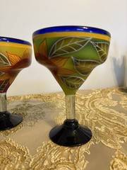 A pair of hand-painted glass margarita glasses with floral and leaf motifs.