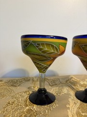 A pair of hand-painted glass margarita glasses with floral and leaf motifs.