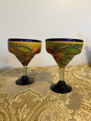 A pair of hand-painted glass margarita glasses with floral and leaf motifs.